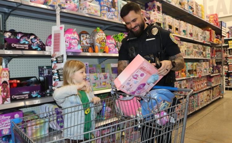Kylin Barwick, 7, gets a smile from Lake City police officer Kevin Johnson as she tells him about a toy she plans to purchase during the Shop With A Cop event on Wednesday morning at Walmart. (TONY BRITT/Lake City Reporter)