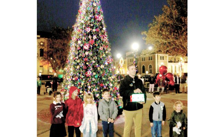 Lake City Mayor Noah Walker is helped by Sierra Lacy (from left), Ariah Leonard, Willow Leonard, Liam Villamil and Legend Brown in lighting the Christmas tree in downtown Olustee Park on Monday night. (TONY BRITT/Lake City Reporter)