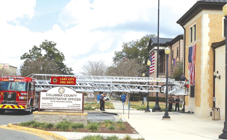 Lake City Fire Department firefighters use their Tower 1 truck to hang the American Flag on the Columbia County Commission Annex Building on Saturday morning. (TONY BRITT/Lake City Reporter)