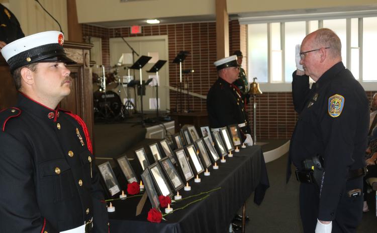 Lake City police officer Greg Burnsed salutes pictures of fallen first responders after placing a flower in honor of them at last year’s Public Safety Memorial. (FILE)