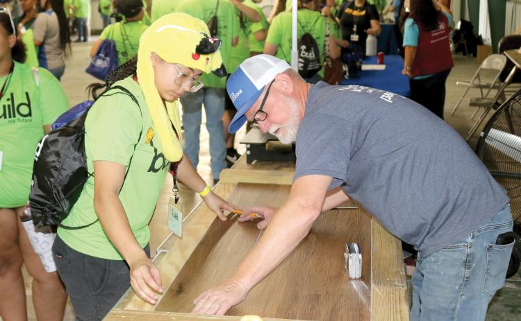 Maylianne Vazquez (left) works on connecting pieces of flooring with Eric Adams of Eric’s Flooring during Wednesday’s Build My Future event. (TONY BRITT/Lake City Reporter)