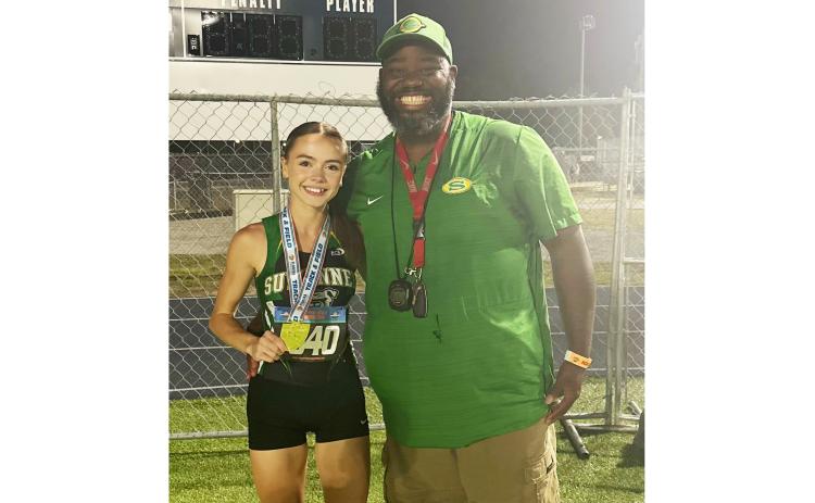 Suwannee senior Ryleigh Hermanson shows off her Class 2A state championship medal in the 1600m alongside assistant coach Twon Williams on Thursday. (COURTESY)