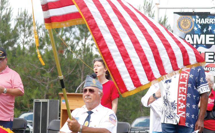 Joy Geiger sings the national anthem during Monday’s Memorial Day ceremony at the American Legion Harry C. Gray II Memorial Post 107 in McAlpin as the American flag waves in front of her. (JAMIE WACHTER/Lake City Reporter)