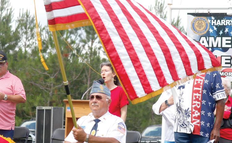 Joy Geiger sings the national anthem during Monday’s Memorial Day ceremony at the American Legion Harry C. Gray II Memorial Post 107 in McAlpin as the American flag waves in front of her. (JAMIE WACHTER/Lake City Reporter)