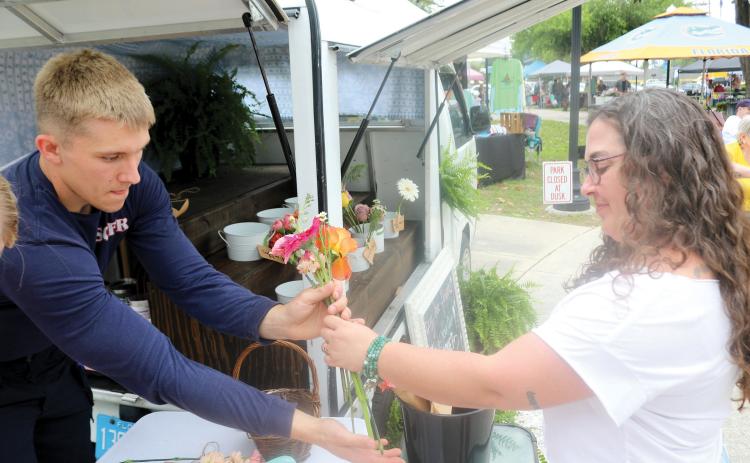 Kaiden Flint (from left) helps Jaime Greenwood as she makes a purchase from the Early Bird Flower Truck during the Spring Market and Multi-Cultural Day event. (TONY BRITT/Lake City Reporter)