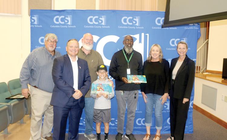 The Lake City Reporter’s Tony Britt accepts the paper’s license plate during the Kids Tag Art presentation. The plate was drawn by Pinemount Elementary’s Jai Bass. (COURTESY)