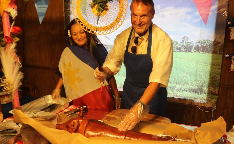Mayla Beaty (left), the incoming president of Filipino-American Cultural Society of Lake City, stands with the Peter Howell as he prepares to cut the roasted pig during the Philippine Independence Day celebration at Quail Heights Country Club on Saturday. (TONY BRITT/Lake City Reporter)