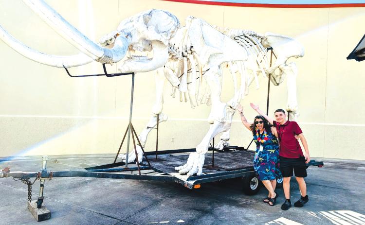 A couple of people pose under the replica mastadon skeleton that was on display at the Columbia County Public Library during a summer kickoff event on Friday. (COURTESY)