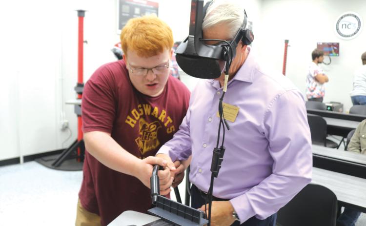 Brody Hoffman (left), a Florida Gateway College student, helps Mitchell Maione, a coordinator for the FGC physical therapy program, as Maione uses a VR welding simulator during the college’s grand opening for its newly renovated welding technology program on Tuesday afternoon. (TONY BRITT/Lake City Reporter)