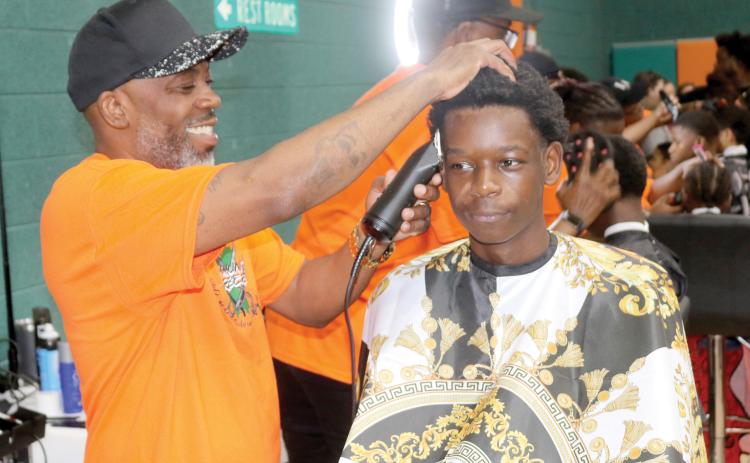 Tyrone Mullins (left), an event organizer for the Community Barbers Back-to-School Bash, gives a youngster a free haircut during last year’s event at the Richardson Community Center. (FILE)