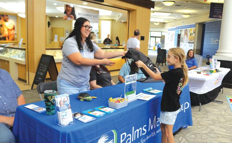 Vivian Jones (from left) of Palms Medical Group gives a book bag to Erin Neal, 10, at the Lake City Mall on Saturday during the Movin’ and Groovin’ Back to School event. (TONY BRITT/Lake City Reporter)