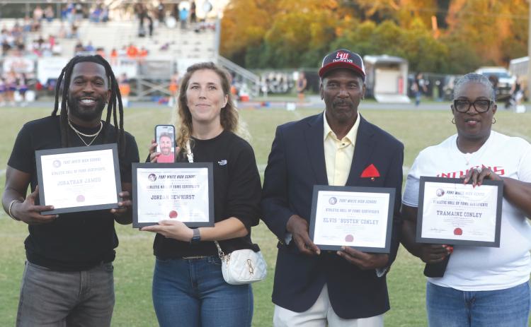 Fort White Hall of Fame inductees Jonathan James (left), Jordan Dewhirst (on phone), Elvis ‘Buster’ Conley and Tramaine Conley were honored with plaques ahead of Friday’s football game against Taylor County. Tramaine Conley, who passed in 2022 at age 38, is represented by his mother, Phyllis Conley. Former baseball player Tyler Shelnut, who was also inducted into the Hall of Fame, could not attend. (MORGAN MCMULLEN/Lake City Reporter)