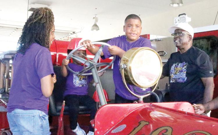 De’ Mari Jackson (third from left), grabs the steering wheel on the antique fire truck as the Lake City Department during a  visit Thursday. Jackson, who has Kleefstra Syndrome, visited the LCFD on Kleestra Syndrome Awareness Day. (TONY BRITT/Lake City Reporter)