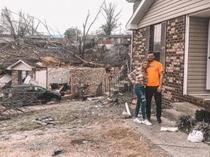 Tori Jackson Tyler and her husband, Mason, stand amidst debris in front of their home — damaged but still left standing by a tornado early Tuesday. (COURTESY)
