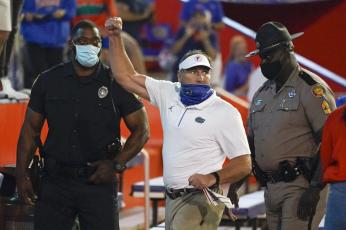 Florida head coach Dan Mullen, center, raises his fist to cheering Florida fans after an argument at the end of the first half as he was escorted to the locker room by law enforcement officers during Saturday's game against Missouri in Gainesville. (JOHN RAOUX/Associated Press)