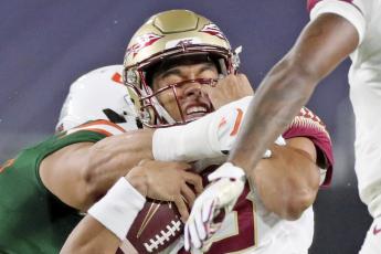 Florida State quarterback Jordan Travis (13) is tackled by a Miami player on Sept. 26 in Miami Gardens. (AL DIAZ/Miami Herald via AP)