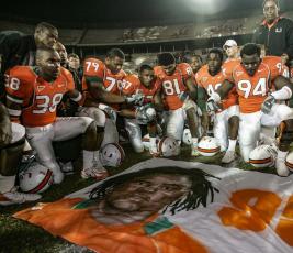 Miami players, including Rashaun Jones (38) at left, pay their respects as they gather around a mural of teammate Bryan Pata after a game against Boston College on Nov. 23, 2006, in Miami. (AL DIAZ/Miami Herald via AP)