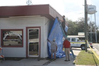 Mayo Laundromat owner Micah Hart staples a tarp to the outside of his business Tuesday afternoon after a semi crashed into the building, and pushed other vehicles through it, Tuesday morning. (MORGAN MCMULLEN/Lake City Reporter)