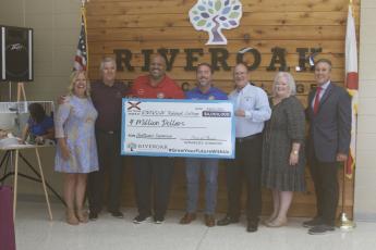 Sen. Corey Simon (red shirt) and Rep. Jason Shoaf (blue shirt) present a ceremonial $4 million check to Suwannee County Superintendent Ted Roush on Tuesday for an expansion at RIVEROAK Technical College. Also present were Karin Hoffman from Key Innovative Solutions (from left), Suwannee County School Board Chairman Jerry Taylor, RIVEROAK Principal Mary Keen and former Sen. Rene Garcia. (JAMIE WACHTER/Lake City Reporter)