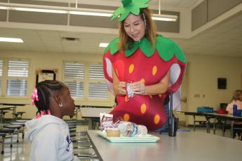 Westside Elementary School Principal Jennifer Saucer opens a carton of milk for a student Friday morning. Saucer was wearing the strawberry costume as part of National School Luncheon Week. (TONY BRITT/Lake City Reporter)