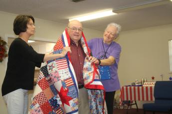Terry Demott (center), a US Army veteran who served in the Vietnam War, is draped by Dianne Shepherd and Fran Vogt on Wednesday morning at a Quilts of Valor ceremony.  The quilts were made by the Lady of the Lake Quilt Guild members. (TONY BRITT/Lake City Reporter)
