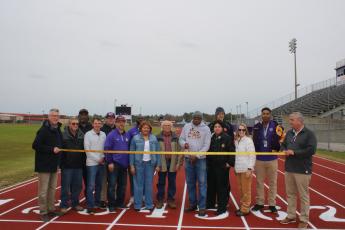 Columbia County School District administrators, Columbia County School Board members and Columbia High School representatives look on as CHS track coach Lawrence Davis cuts the ribbon Monday to officially open the resurfaced track at Tiger Stadium. (TONY BRITT/Lake City Reporter)