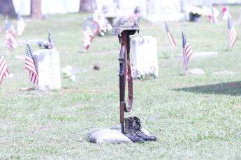 A Battlefield cross sits in the Veterans Memorial section of the Live Oak Cemetery during the Memorial Day service Monday as flags adorn the graves of the veterans buried there. (JAMIE WACHTER/Lake City Reporter)