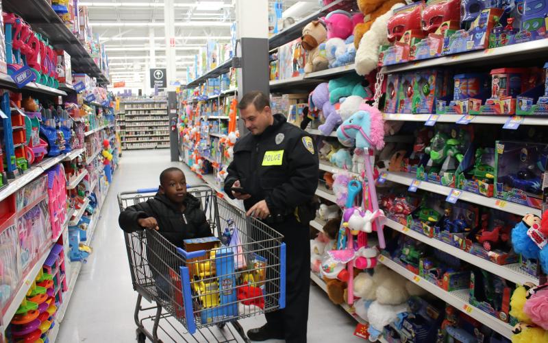 Zae’len Douglas, 5, sits in a shopping cart with the toys he plans to buy as he tells LCPD officer Brandon Colbert what he wants to buy next. (TONY BRITT/Lake City Reporter)