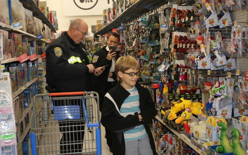 LCPD officer Gregory Burnsed and Edward Arnold, 9, look  at Pokemon and Toy Story 4 toys while shopping Wednesday morning, as Lake City Police Department’s community relations coordinator, Ashely Crews, takes some candid photos. (TONY BRITT/Lake City Reporter)