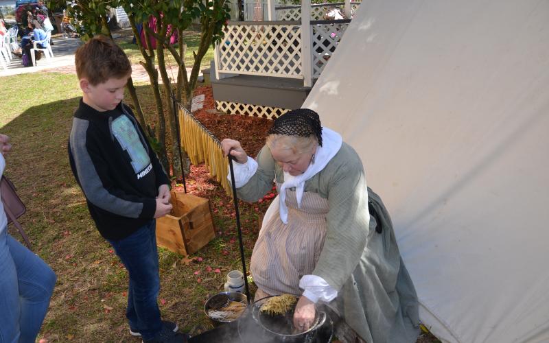 Becky Johnson shows young Aiden Cady some 1860s cuisine. A large bowl of stew simmered nearby, as a group of teen actors performed a brief play at the Lake City-Columbia County Historical Museum around 1 p.m. Saturday. (CARL MCKINNEY/Lake City Reporter)