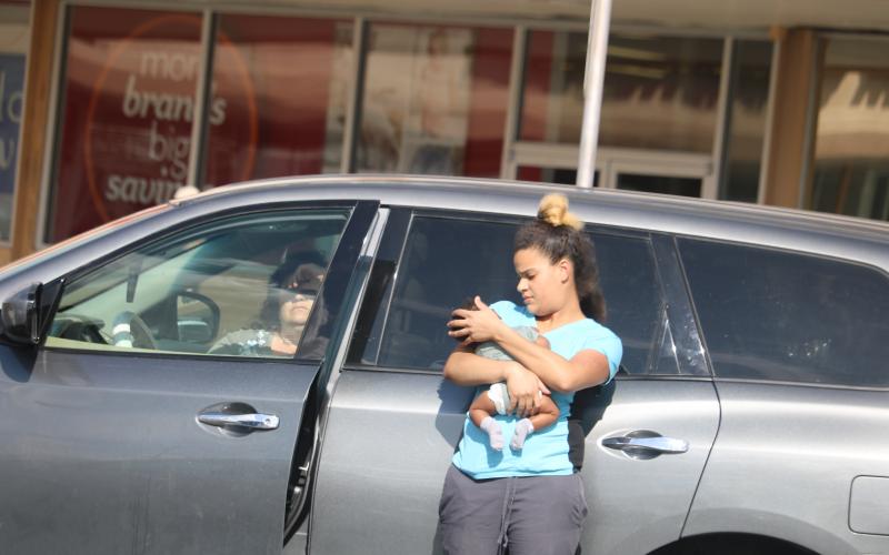 The woman authorities say left a baby unattended in a car Monday afternoon sits in the vehicle at Lake City Plaza as the baby’s mother holds the child. (TONY BRITT/Lake City Reporter)