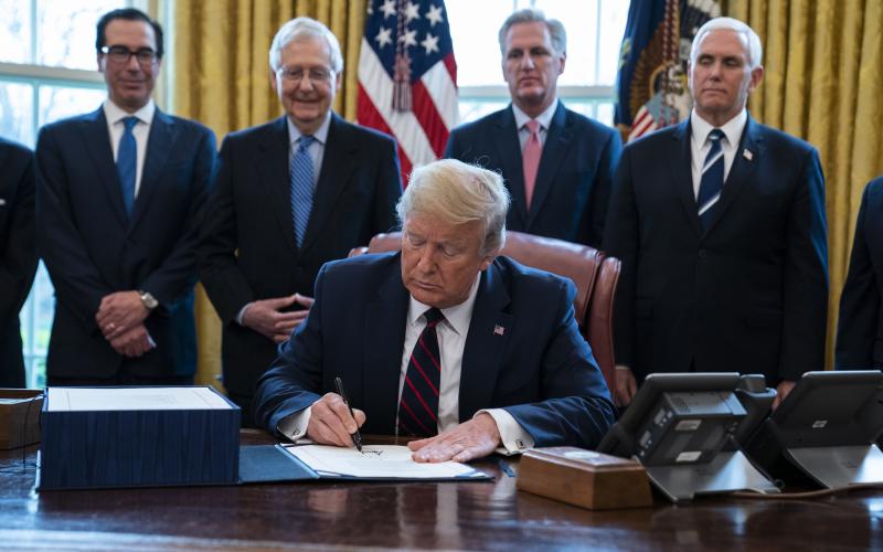President Donald Trump signs the coronavirus stimulus relief package in the Oval Office Friday. (AP PHOTO)