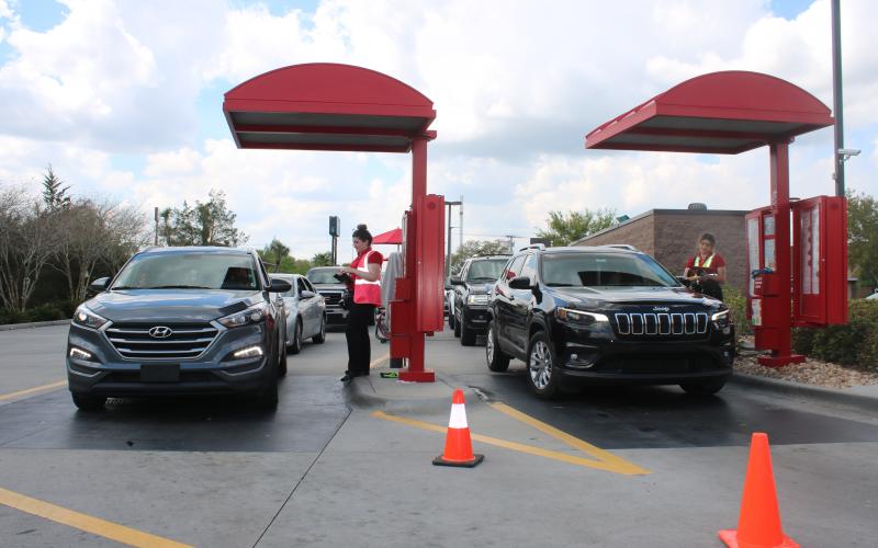 Chick-fil-A employees take orders and payment from customers Wednesday afternoon as patrons form a line in their vehicles. The eatery is not allowing customers in its dining room and only providing drive through services because of the COVID-19 global pandemic. (TONY BRITT/Lake City Reporter)