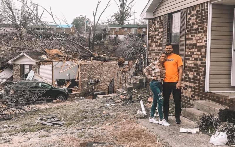 Tori Jackson Tyler and her husband, Mason, stand amidst debris in front of their home — damaged but still left standing by a tornado early Tuesday. (COURTESY)