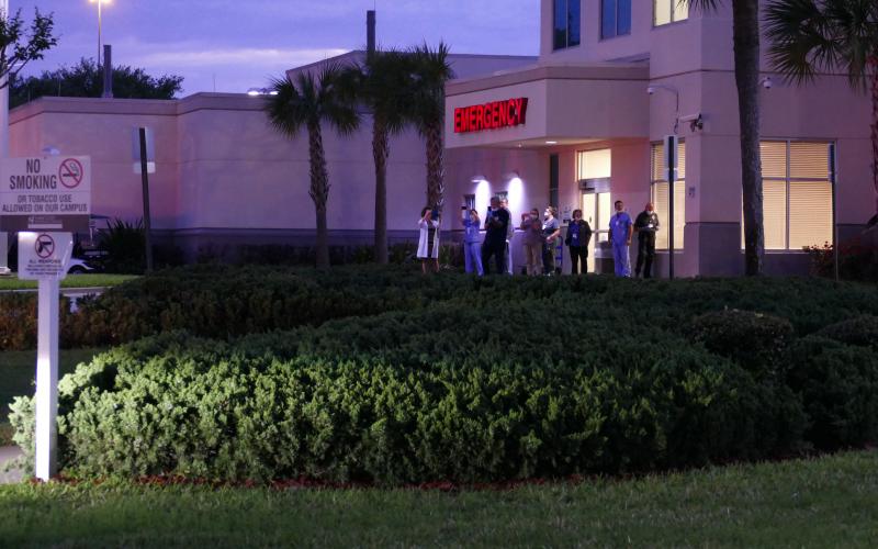 Hospital workers stand near the emergency room entrance, looking on as a group of people prayed separately in their vehicles. (TRAVIS LEE/Special to the Reporter)