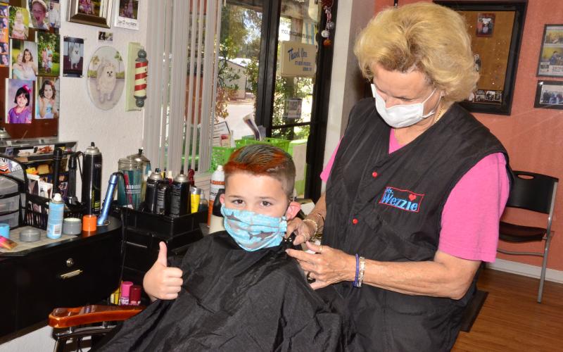 Louise Huelskamp, better known as “Miss Wezzie,” puts the finishing touches on 8-year-old Hagan Stalvey, who also asked for a touch of pink coloring in his hair.         As the state continues relaxing quarantine restrictions, hair salons and barber shops were allowed to reopen on Monday. (CARL MCKINNEY/Lake City Reporter)