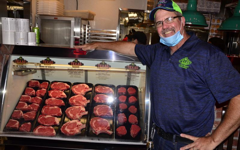 Steve Hale, managing partner for the Lake City Texas Roadhouse, poses alongside an assortment of meats ahead of the opening of the chain’s new location. (CARL MCKINNEY/Lake City Reporter)