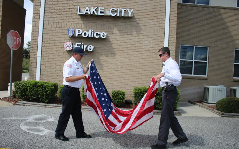 Josh Wehinger, (from left) Lake City Fire Department assistant chief and Andy Mangrum, a Lake City Police Department investigator, fold the American Flag after a brief 9/11 memorial ceremony rehearsal Wednesday afternoon at the city’s Public Safety building. (TONY BRITT/Lake City Reporter)