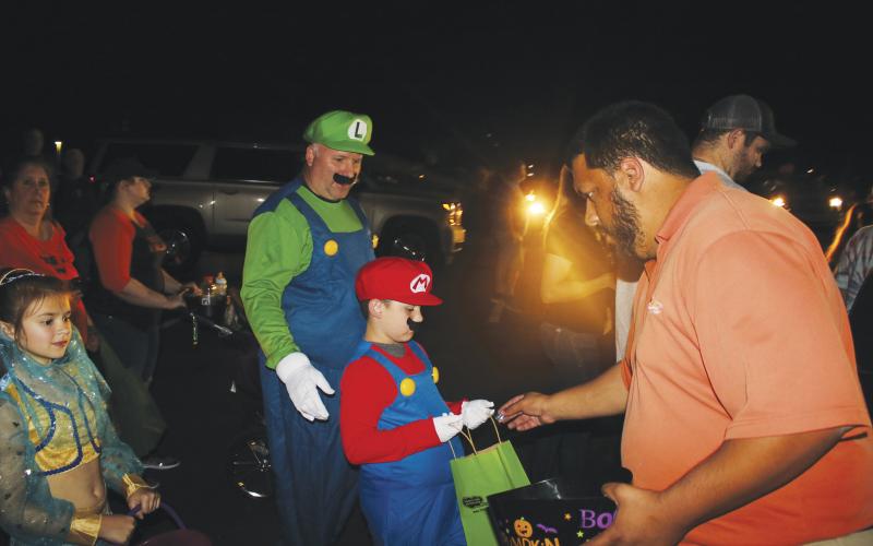 Robert Stalvey and Hagan Stalvey, 7, came dressed as Luigi and Mario at last year’s Trunk or Treat. Here Hagan accepts candy from Steven Flores. (FILE)