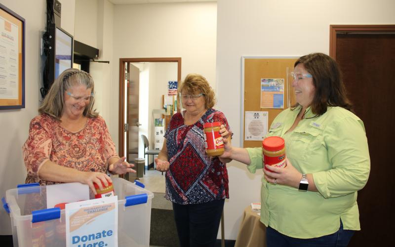Julia Fulton (from left), county extension service secretary specialist, gets jars of peanut butter from Garnet Dasher, county extension service secretary specialist, and Heather Janney, UF/IFAS Extension Columbia County Extension director and 4H agent, on Tuesday afternoon as they collect peanut butter for the Peanut Butter Challenge. (TONY BRITT/Lake City Reporter)