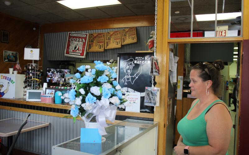 Caryn Cooper, daughter of the late Robert Warren Cooper Jr., who was the owner of the Pizza Boy Pizza restaurant, looks at a bouquet of flowers on the restaurant’s counter Wednesday afternoon. (TONY BRITT/Lake City Reporter)