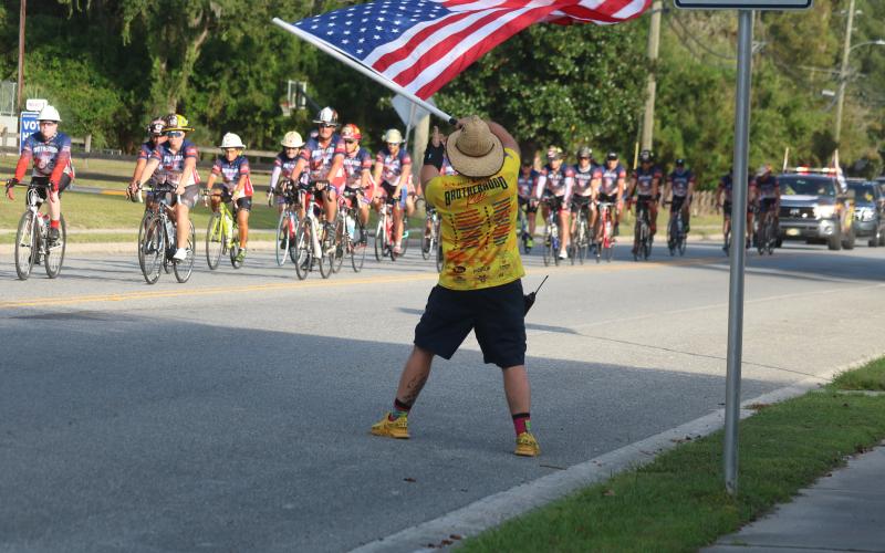 Zak Jones with the North Collier Fire Department waves an American flag Wednesday evening as dozens of Brotherhood Ride cyclists end their week-long trek across Florida at the Live Oak Fire Department station. The Brotherhood Ride is an annual bike ride to honor first responders who died in service. Former Suwannee County Fire Chief James Sommers was among those honored this year. Sommers died in August 2019. (JAMIE WACHTER/Lake City Reporter)