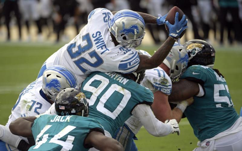 Detroit Lions running back D'Andre Swift (32) leaps over Jacksonville Jaguars linebacker Myles Jack (44) and defensive tackle Taven Bryan (90) for a touchdown on Oct. 18 in Jacksonville. (PHELAN M. EBENHACK/Associated Press))