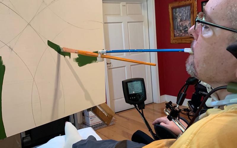Peter Herrick, a tetraplegic combat veteran from Fort White, paints using a modified paintbursh and a rotating easel. He is the November featured artist at the Gateway Art Gallery. (COURTESY)