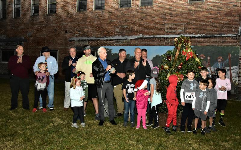 Live Oak Mayor Frank Davis, surrounded by city, Suwannee County and Suwannee County Chamber of Commerce officials as well as participants in the Jingle Bell Fun Run, lights the heritage Christmas tree in Festival Park on Thursday night to open the Christmas on the Square festivities. (ROB WOLFE/Special to the Reporter)
