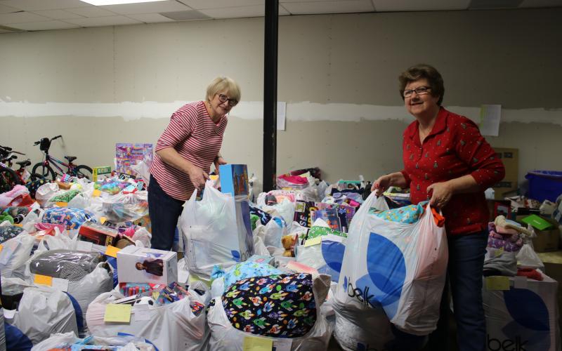 Meally Jenkins  (left), Christmas Dream Machine executive director and founder, and Janet Stanford, a Christmas Dream Machine director, move bags of gift bags as they prepare for the organization’s toy distribution. (TONY BRITT/Lake City Reporter)