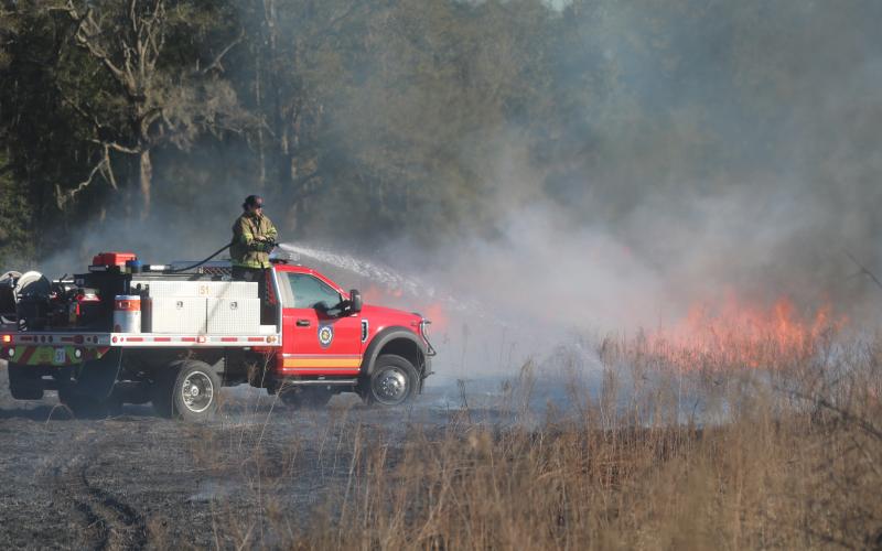 An unidentified firefighter with Columbia County Fire Rescue stands on the back of a brush truck while spraying water on a brush fire Tuesday afternoon. (TONY BRITT/Lake City Reporter)