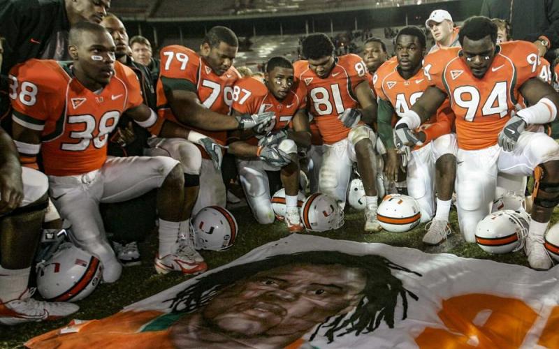 Miami players, including Rashaun Jones (38) at left, pay their respects as they gather around a mural of teammate Bryan Pata after a game against Boston College on Nov. 23, 2006, in Miami. (AL DIAZ/Miami Herald via AP)