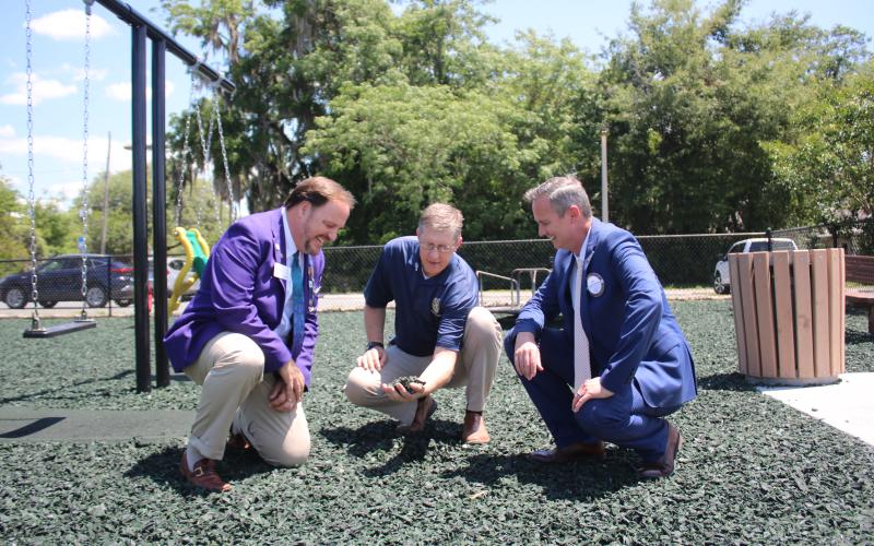 District Rotary Governor Dan Sulger (left), Rotary Club of Lake City President Jay Swisher (right) and Lake City Rotarian John Wheeler take a closer look at the rubber mulch that replaced sand at the Rotary Children’s Playground at downtown Wilson Park. (TONY BRITT/Lake City Reporter)