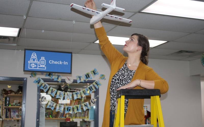 Kate Duong, the Youth Services Outreach Librarian for the Columbia County Public Library, hangs an airplane at the Main Branch library Wednesday. The library’s summer rading program is travel themed, providing information on six of the seven continents. (TONY BRITT/Lake City Reporter)